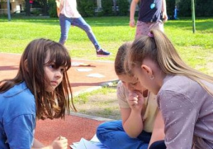 dziewczynki siedzące nad zielonymi kartkami